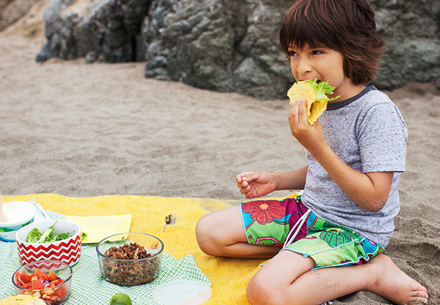 Boy on a beach blanket eating tacos